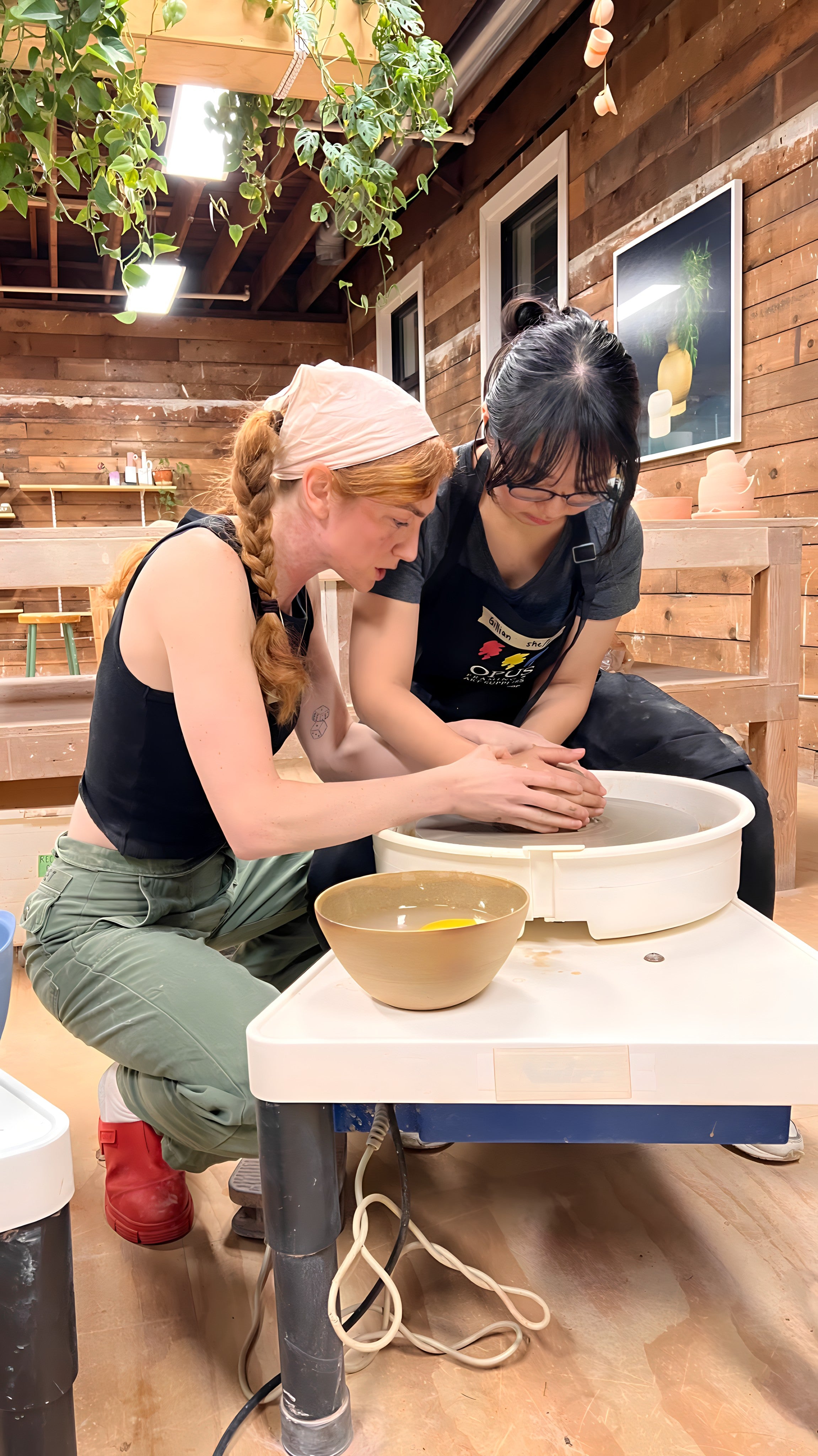 Pottery instructor with a student in our beginners whee-thwoing workshop learning how to center.